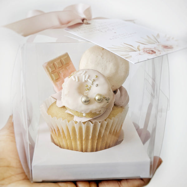 Cupcake in a clear box held by a hand on a white background