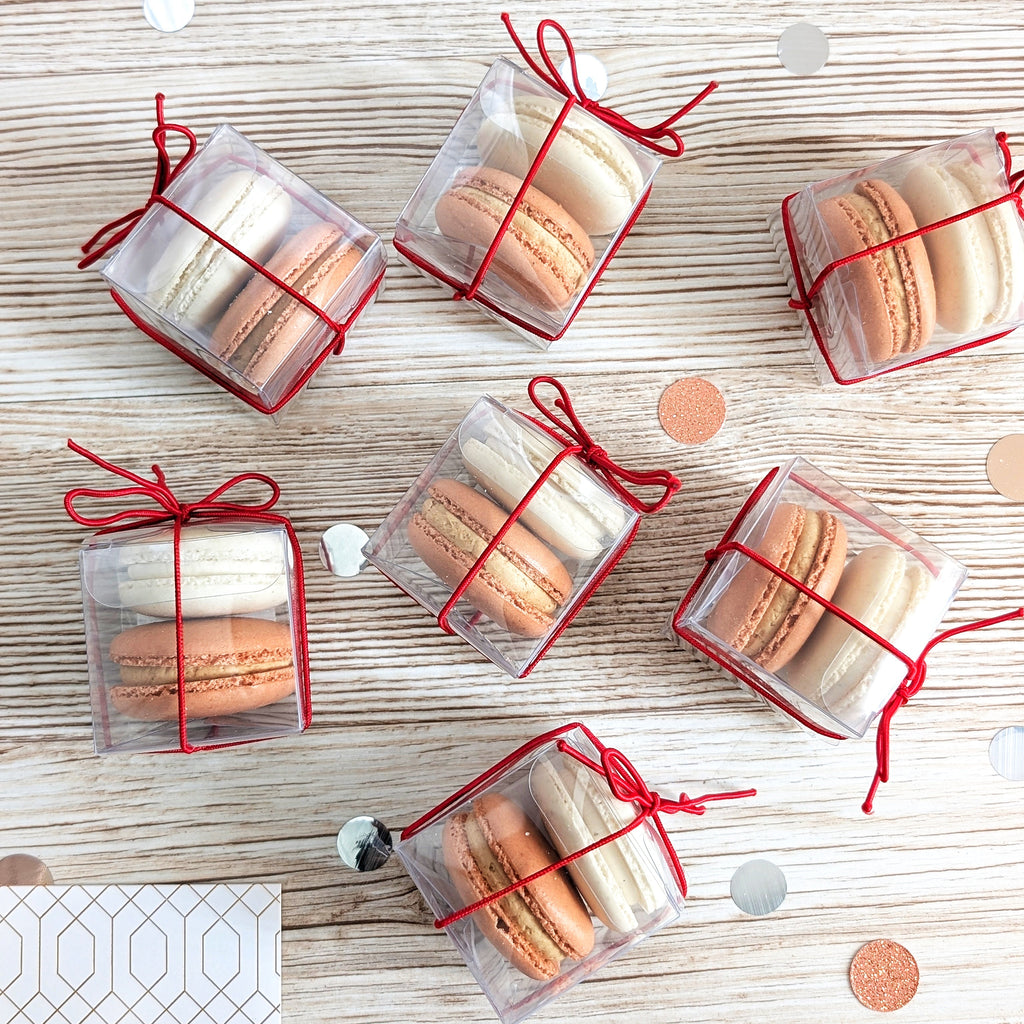 Macarons in clear packaging with red ribbons on a wooden surface